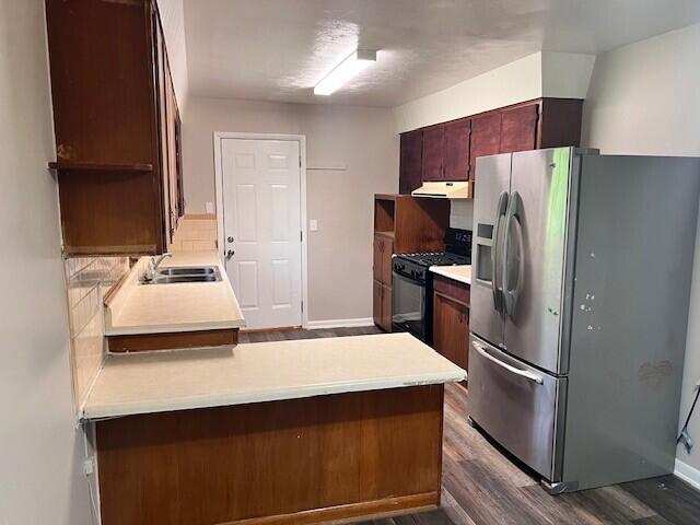 kitchen with dark wood-style flooring, stainless steel fridge, a sink, black range with gas cooktop, and under cabinet range hood