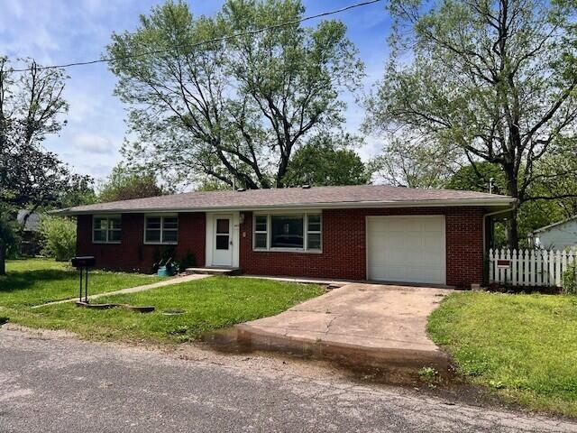 ranch-style home with driveway, brick siding, fence, a front lawn, and an attached garage