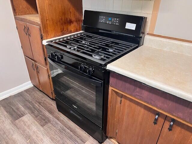 kitchen with brown cabinetry, baseboards, light wood-style floors, light countertops, and black gas range oven