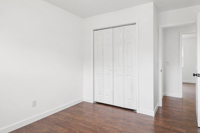 unfurnished bedroom featuring baseboards, dark wood-style floors, and a closet