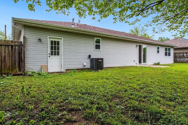 rear view of property featuring fence, a lawn, and cooling unit