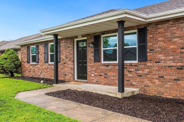 doorway to property featuring a yard, brick siding, and a shingled roof