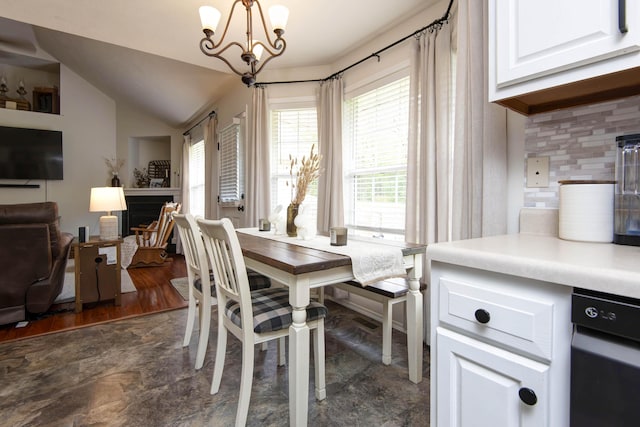 dining room featuring an inviting chandelier, a fireplace, and vaulted ceiling
