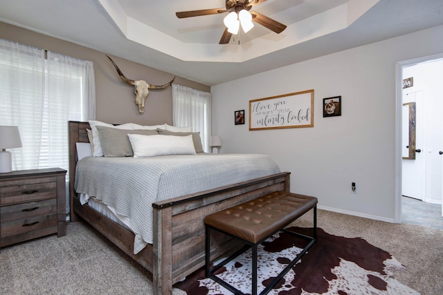 bedroom featuring baseboards, carpet flooring, a raised ceiling, and a ceiling fan