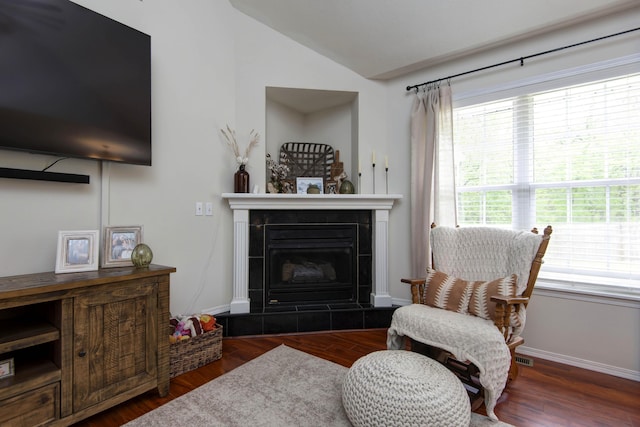 living area with a tiled fireplace, baseboards, wood finished floors, and lofted ceiling