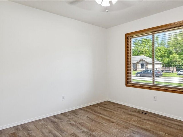 empty room with baseboards, a ceiling fan, wood finished floors, and visible vents