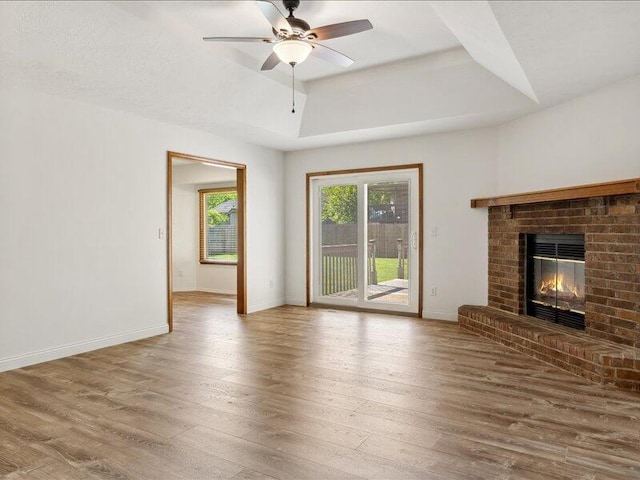 unfurnished living room featuring baseboards, ceiling fan, a fireplace, and wood finished floors