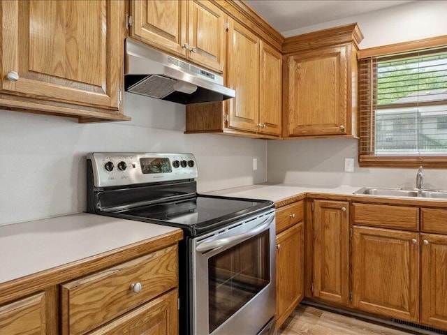 kitchen with brown cabinets, stainless steel electric range, light countertops, a sink, and under cabinet range hood