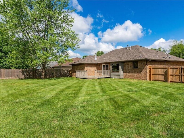 rear view of property featuring a fenced backyard, a lawn, a deck, and brick siding