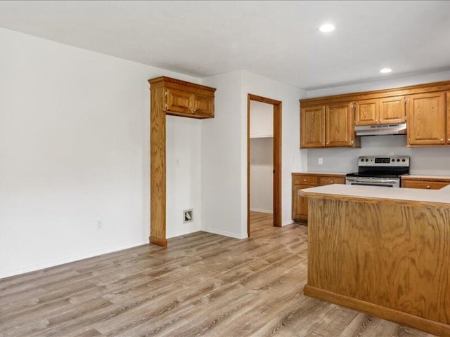 kitchen with stainless steel range with electric stovetop, light countertops, brown cabinetry, light wood-style flooring, and under cabinet range hood