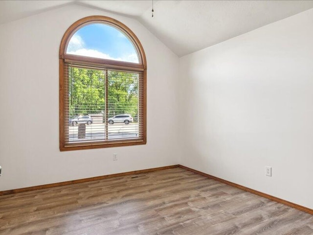 empty room featuring baseboards, vaulted ceiling, and wood finished floors