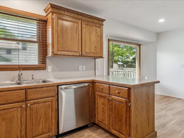 kitchen featuring light wood-type flooring, dishwasher, a sink, light countertops, and a peninsula