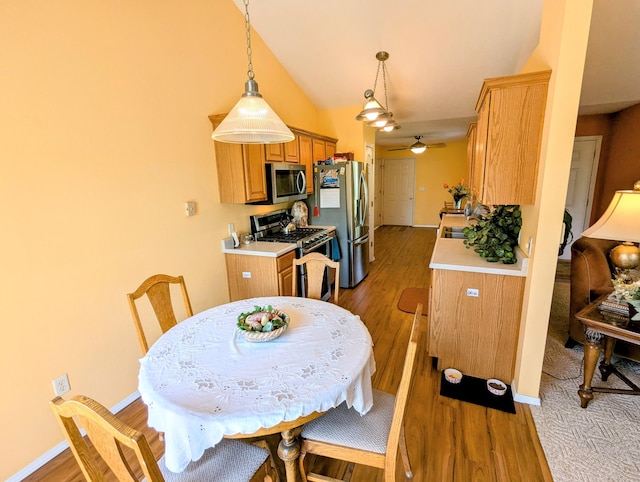 dining room featuring a ceiling fan, baseboards, vaulted ceiling, and light wood finished floors