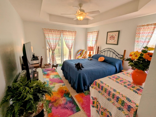 bedroom with access to outside, a tray ceiling, carpet flooring, and ceiling fan