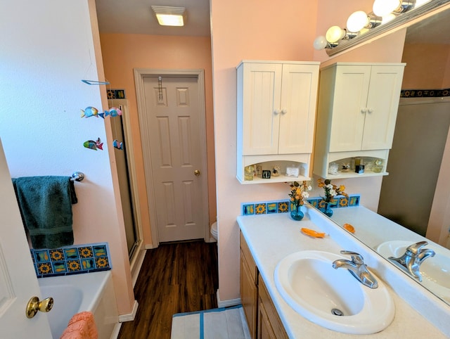 bathroom with a garden tub, a shower with shower door, wood finished floors, vanity, and toilet