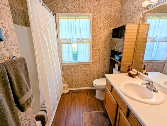 bathroom with toilet, wallpapered walls, plenty of natural light, and wood finished floors
