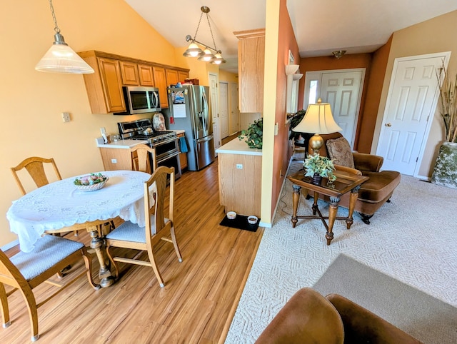 interior space featuring lofted ceiling, light countertops, light wood finished floors, appliances with stainless steel finishes, and decorative light fixtures