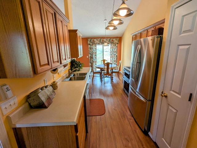 kitchen with brown cabinetry, a sink, light countertops, stainless steel appliances, and light wood-style flooring