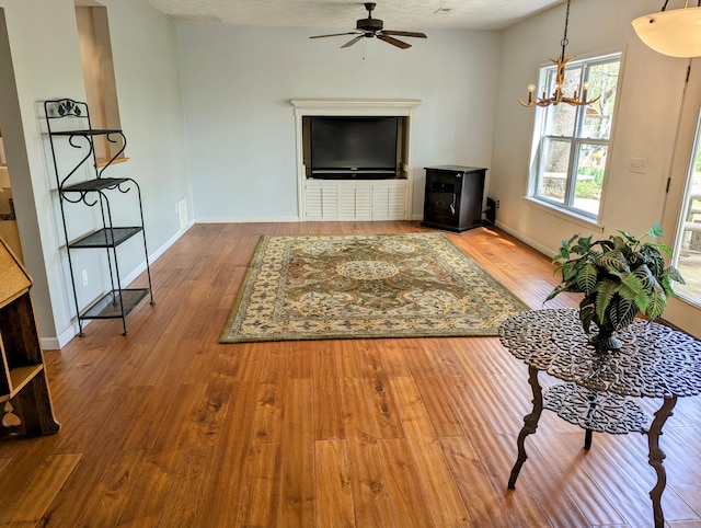 living area featuring baseboards, ceiling fan with notable chandelier, and wood finished floors