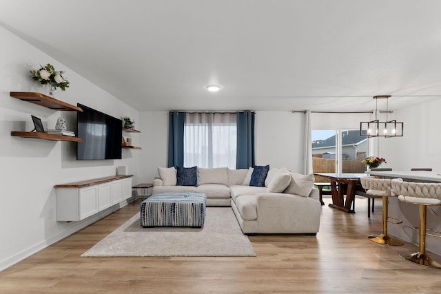 living room featuring light wood-type flooring, baseboards, a wealth of natural light, and an inviting chandelier