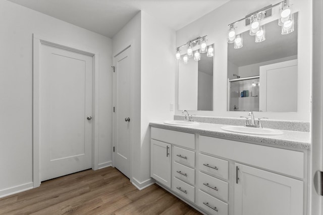 full bathroom with double vanity, a sink, wood finished floors, and a shower stall
