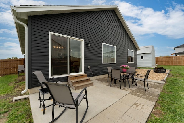 rear view of property featuring a fire pit, fence, a patio, entry steps, and an outbuilding