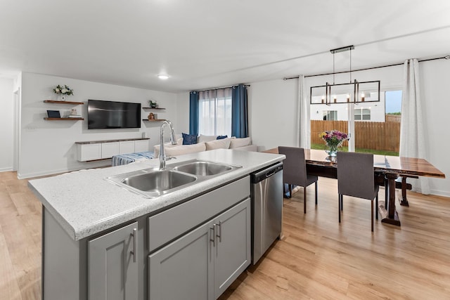 kitchen with a sink, dishwasher, light countertops, gray cabinets, and a center island with sink