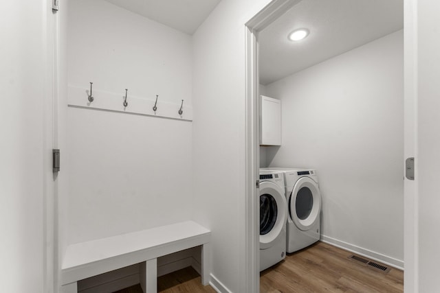 washroom featuring baseboards, light wood-type flooring, cabinet space, and washing machine and clothes dryer