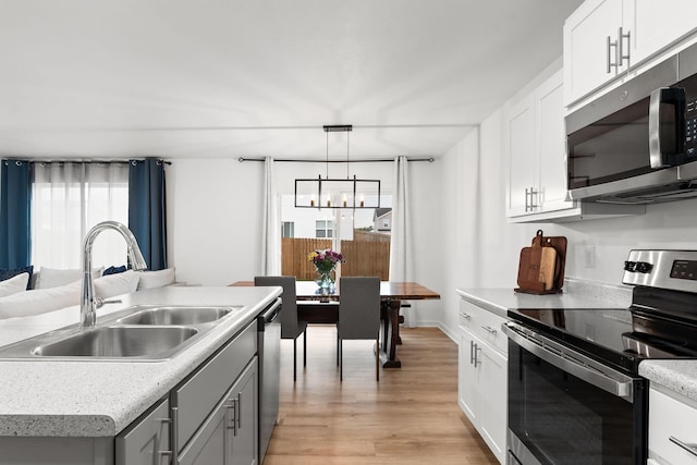 kitchen with a sink, light countertops, an inviting chandelier, stainless steel appliances, and light wood-style flooring
