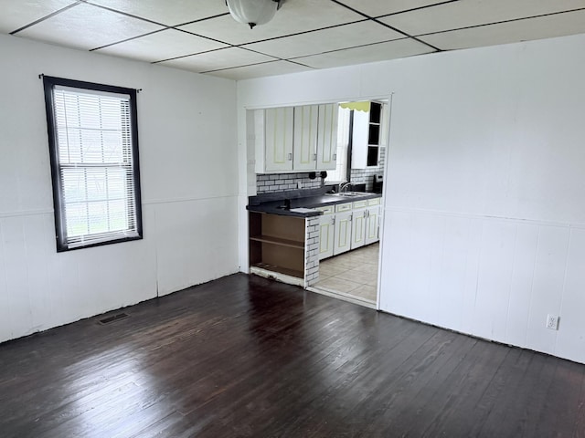 kitchen with a sink, dark countertops, wainscoting, and wood finished floors