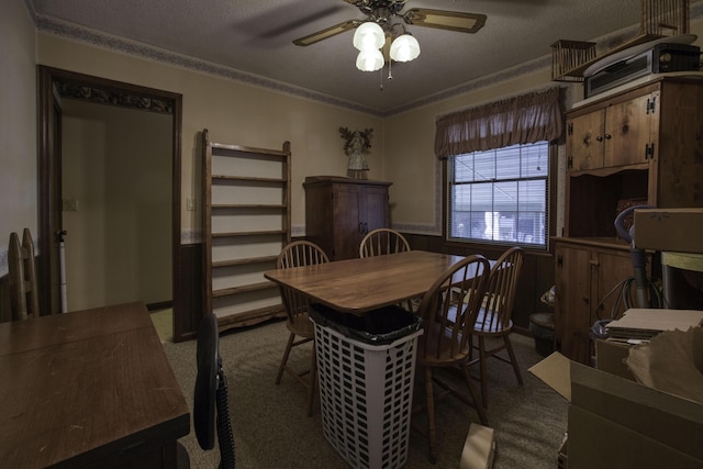 dining room featuring a ceiling fan, a textured ceiling, wainscoting, and dark carpet