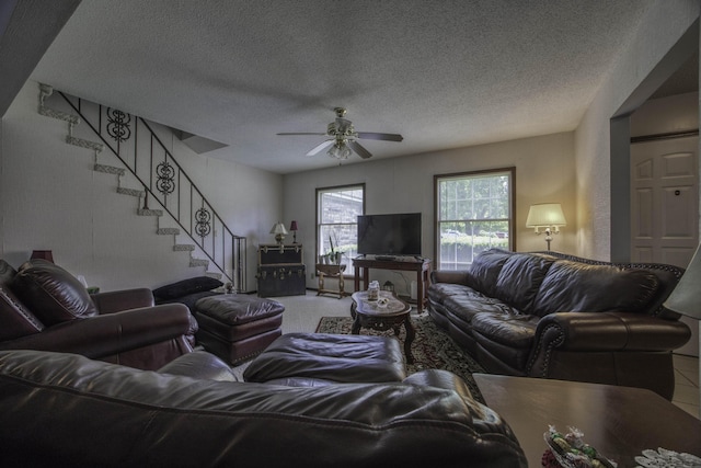 living room featuring a textured ceiling, ceiling fan, and stairway