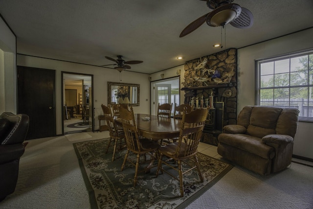carpeted dining room featuring a stone fireplace, ceiling fan, and a wealth of natural light