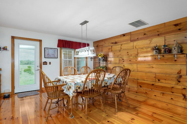 dining room featuring wood walls, hardwood / wood-style flooring, and visible vents