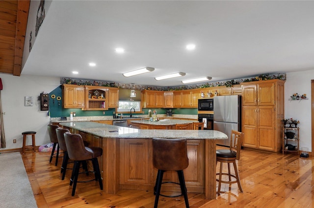 kitchen featuring a breakfast bar area, light stone countertops, a sink, black appliances, and light wood-style floors