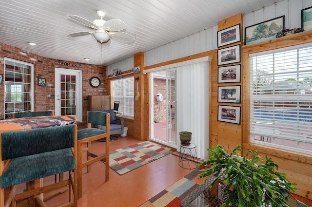 sunroom with outdoor dining space, wood walls, brick wall, and ceiling fan