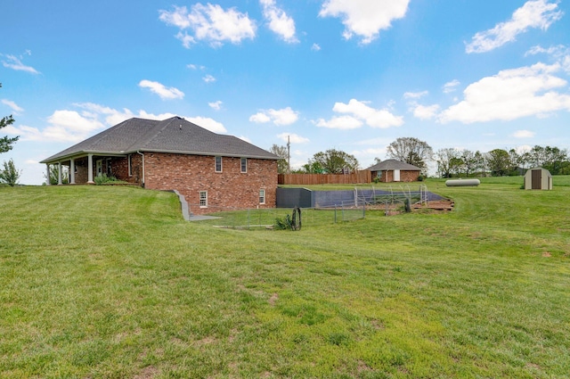 view of side of home featuring fence, a storage unit, brick siding, an outbuilding, and a yard