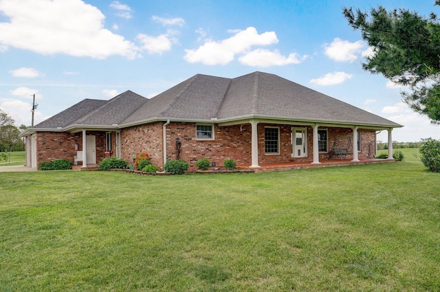 view of front facade featuring a front yard, a shingled roof, brick siding, and covered porch