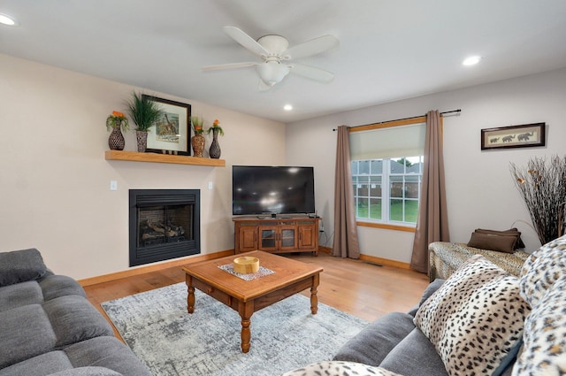 living room with baseboards, ceiling fan, a fireplace, and light wood-type flooring
