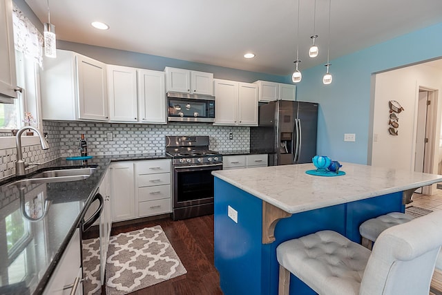 kitchen with appliances with stainless steel finishes, a sink, a breakfast bar, backsplash, and dark wood finished floors