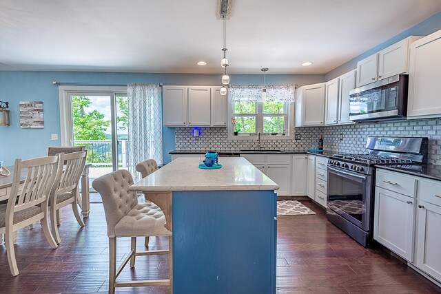 kitchen with stainless steel appliances, a sink, a kitchen island, a breakfast bar area, and dark wood-style flooring