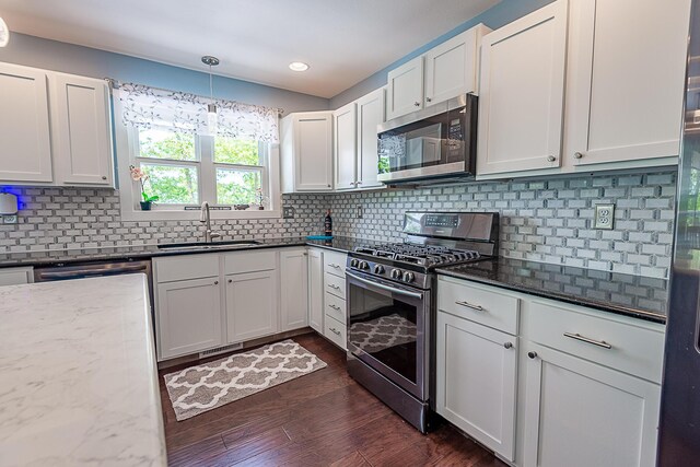 kitchen with stainless steel appliances, a sink, dark stone counters, dark wood-type flooring, and recessed lighting