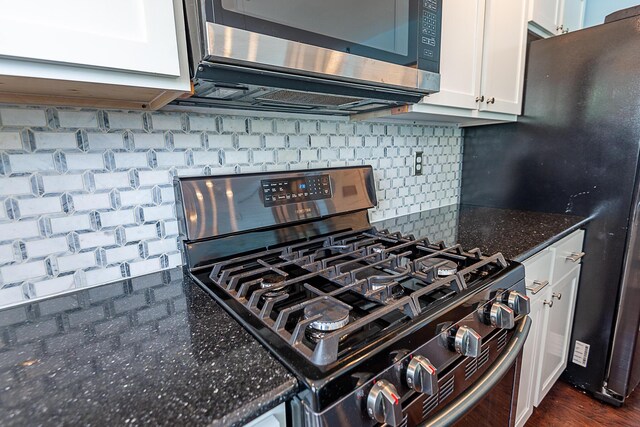 kitchen view of stainless steel appliances, white cabinets, decorative backsplash, and dark stone countertops