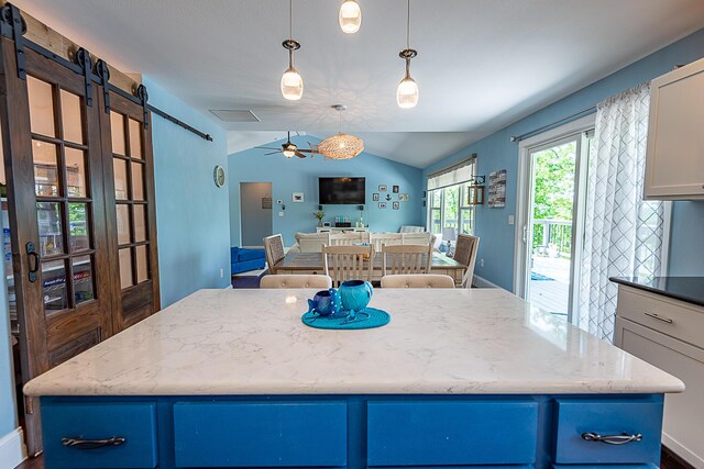 kitchen featuring a barn door, a ceiling fan, lofted ceiling, a center island, and light stone countertops