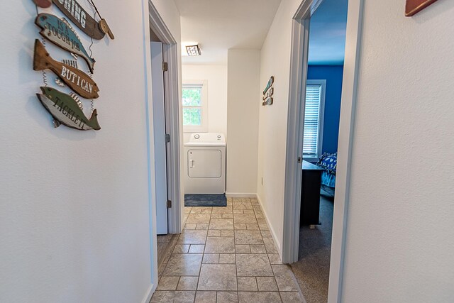 corridor featuring washer / clothes dryer, stone tile flooring, and baseboards