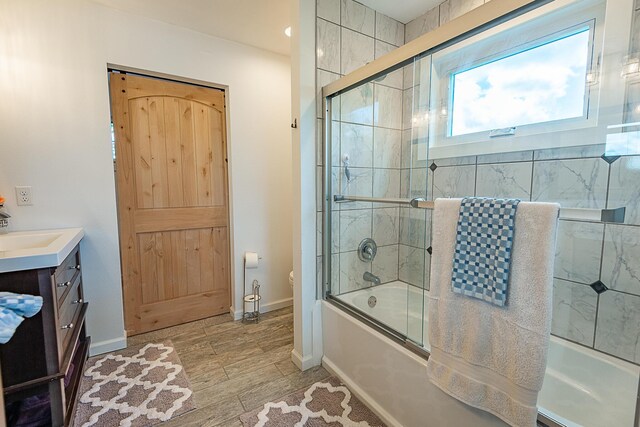 full bathroom with combined bath / shower with glass door, vanity, toilet, and baseboards
