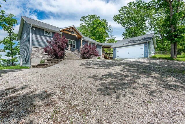 view of front of house with covered porch, gravel driveway, stone siding, and a garage
