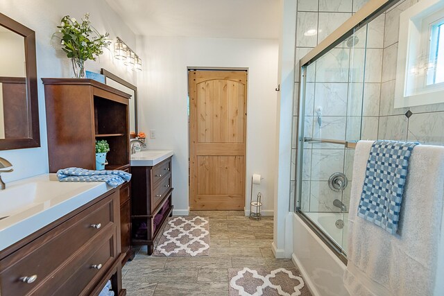 full bathroom with combined bath / shower with glass door, two vanities, and baseboards