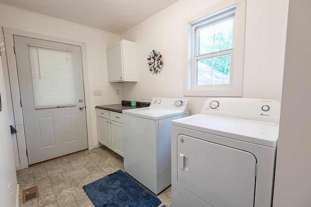 clothes washing area with washing machine and clothes dryer, cabinet space, and stone finish flooring