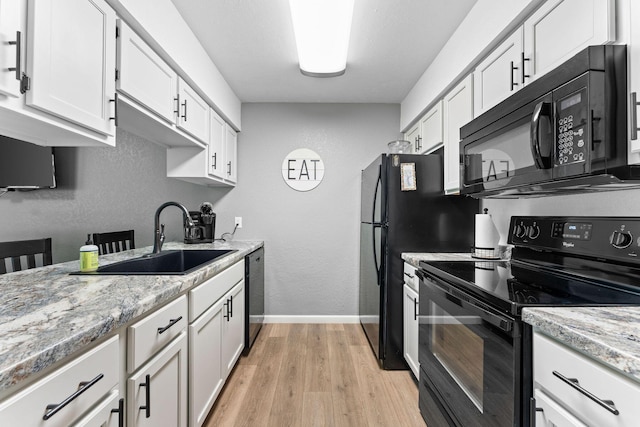 kitchen with a sink, baseboards, white cabinets, black appliances, and light wood finished floors